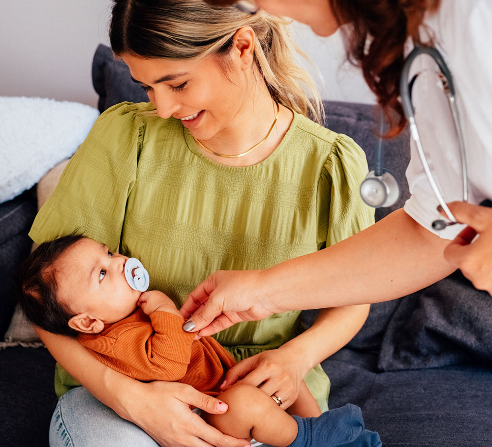 Mother holding baby with pacifier during pediatric checkup at home