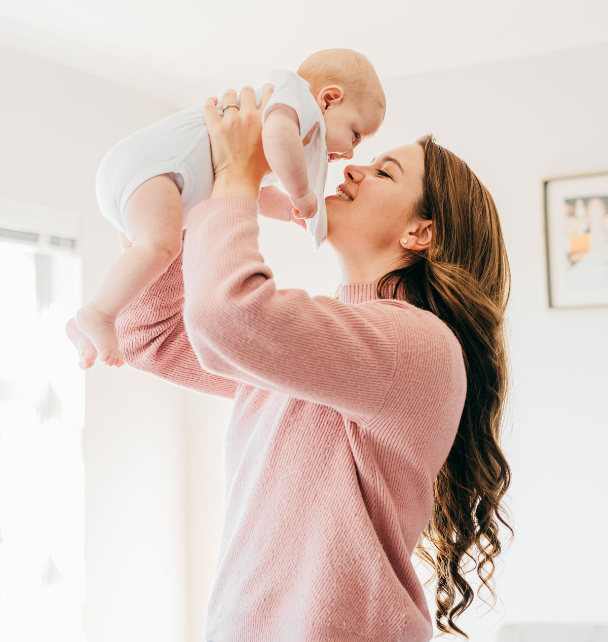 Mother lifting baby in the air and smiling at home