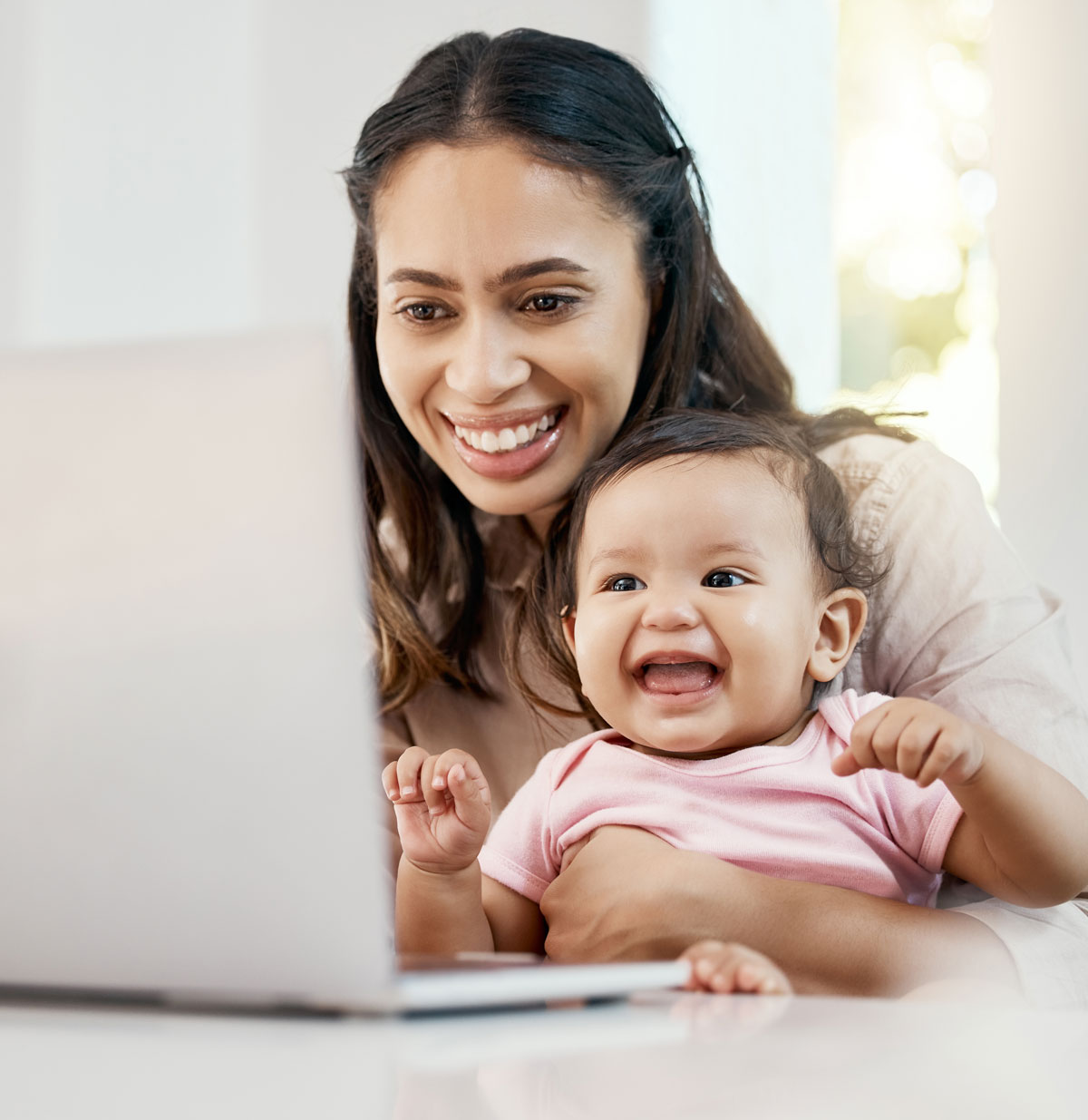 Smiling mother holding baby while using laptop at home