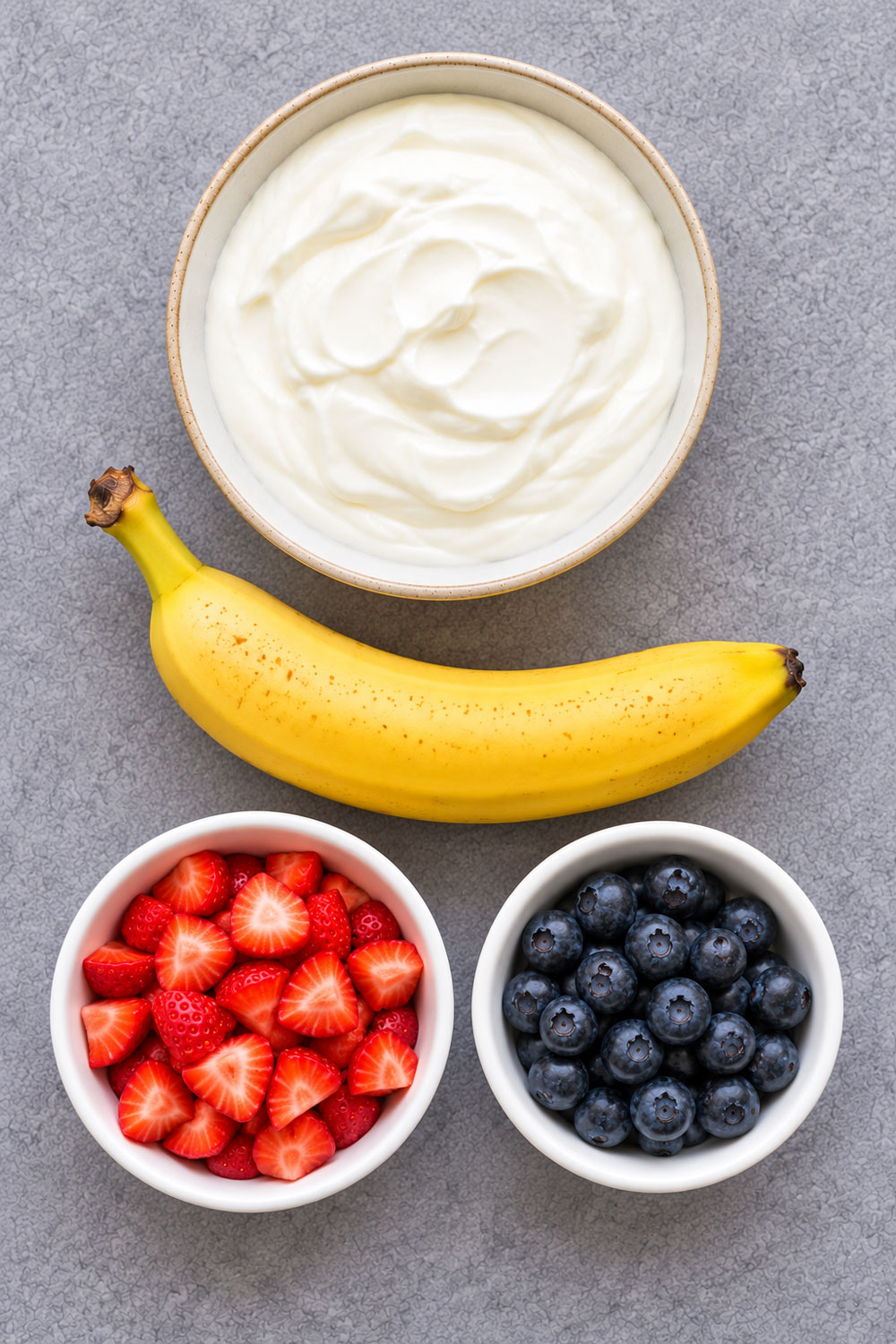 Ingredients for a yogurt fruit snack: yogurt, banana, strawberries, and blueberries