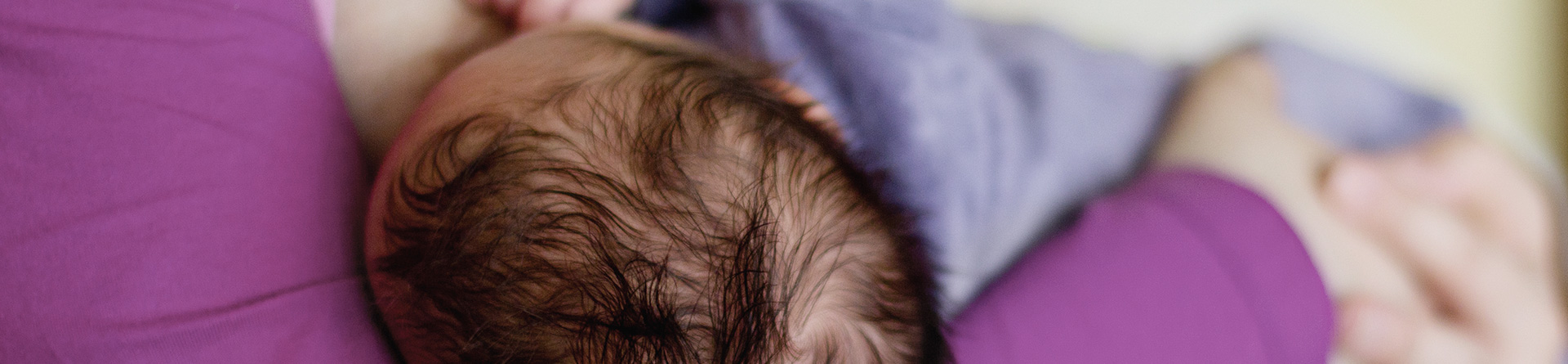 Infant cuddled in arms wearing purple shirt