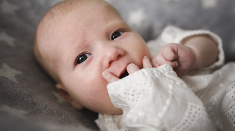 A baby with blue eyes and light skin lies on a soft