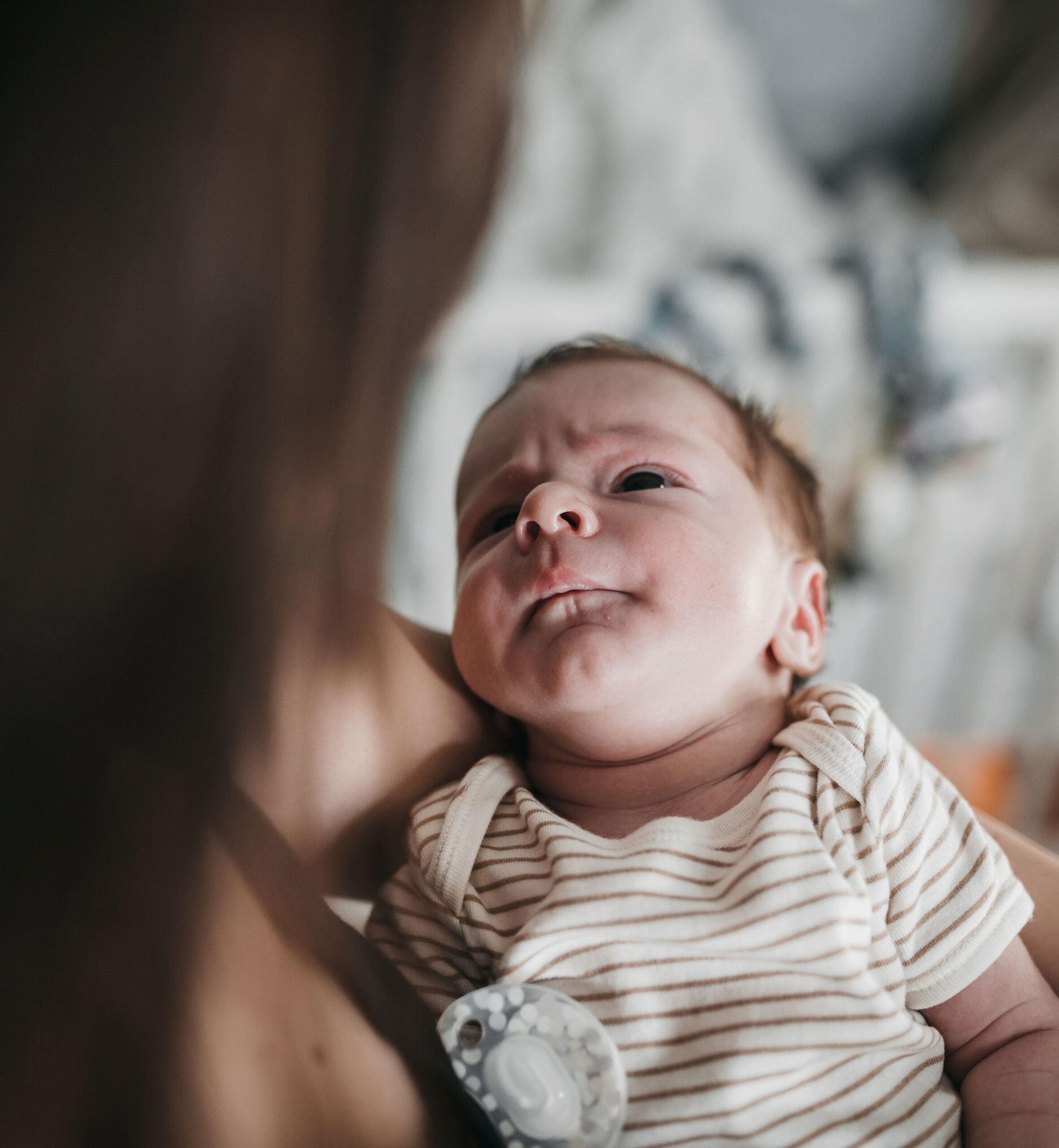 Newborn baby looking up while being held in mother’s arms.
