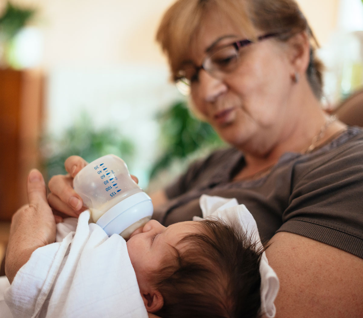 Grandmother feeding a baby with a bottle.
