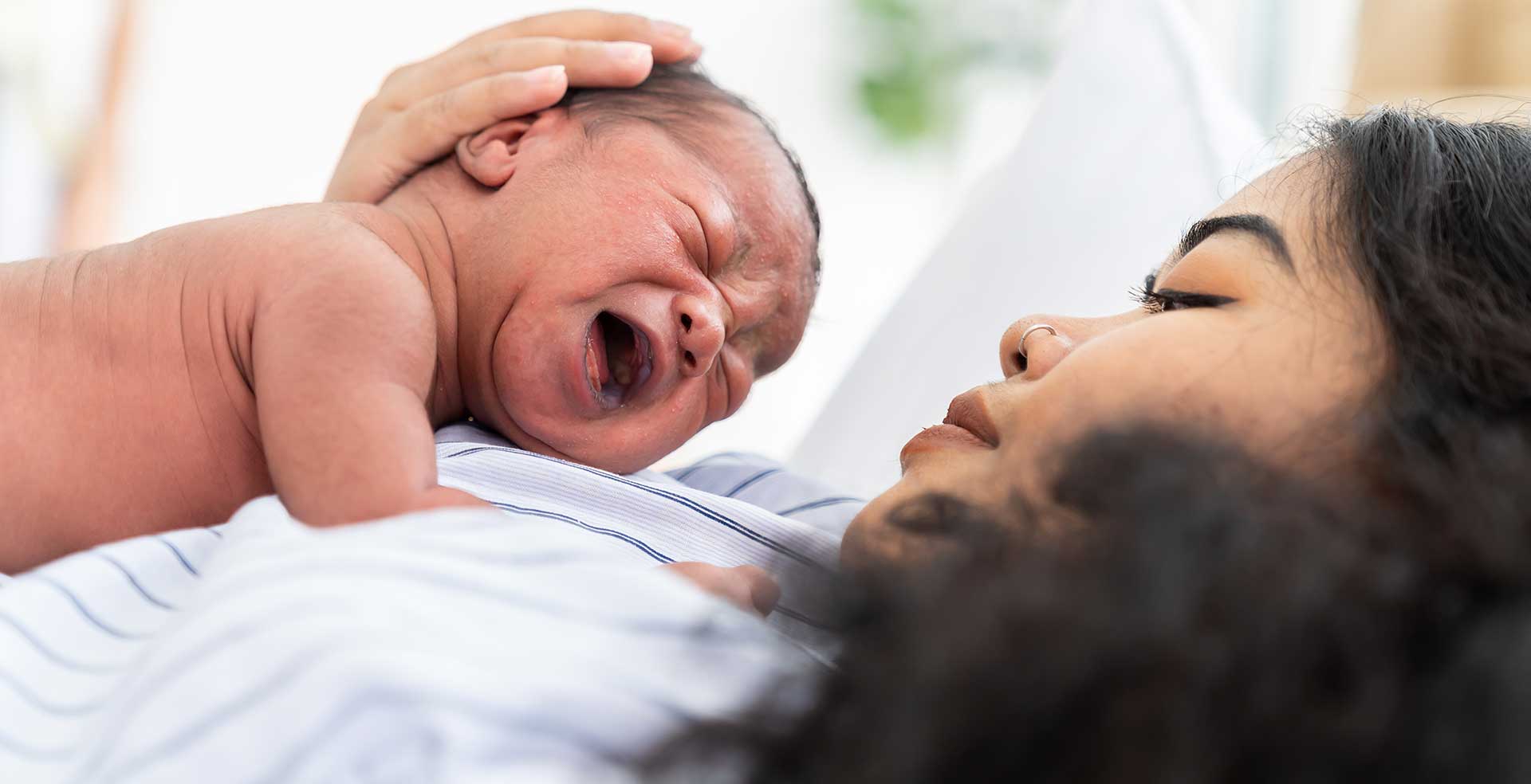 Mother comforting crying newborn baby on chest