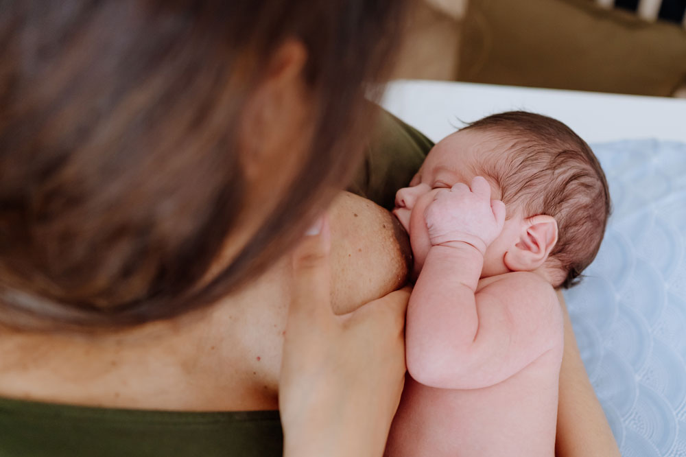 Newborn breastfeeding while resting a hand on mother's chest