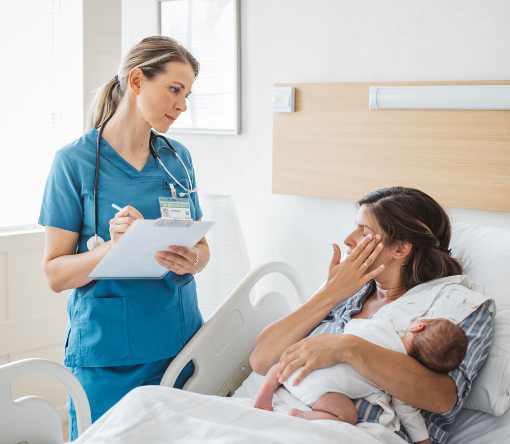 Nurse checking on a mother holding her newborn in a hospital bed