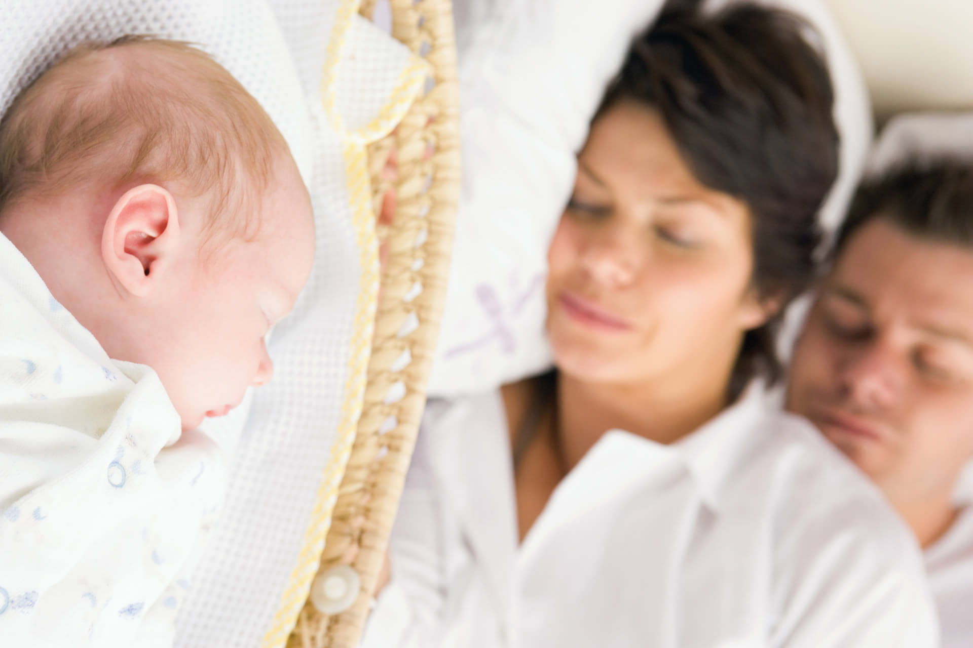 parents sleeping beside baby in basket