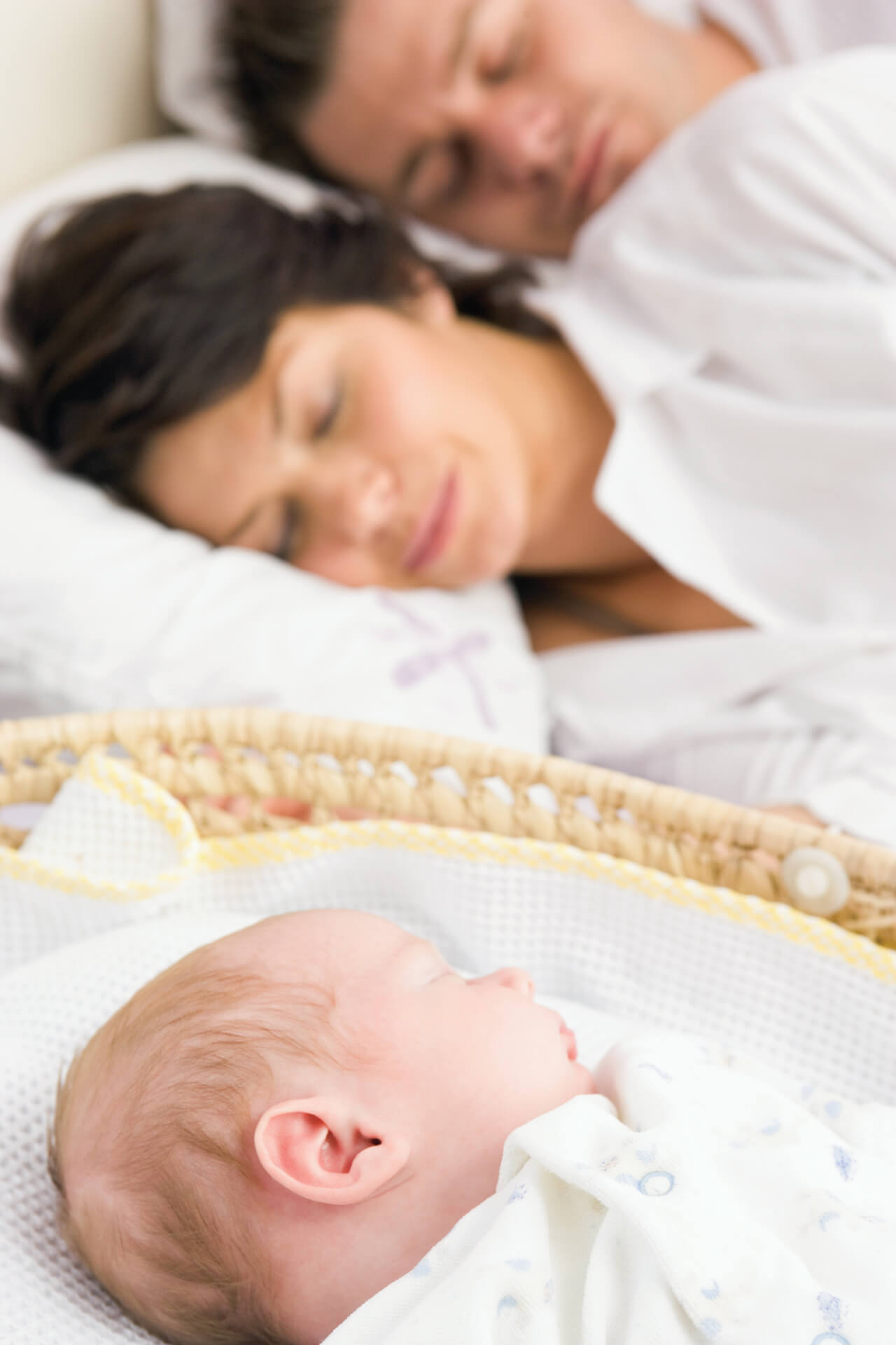 parents sleeping beside baby in basket