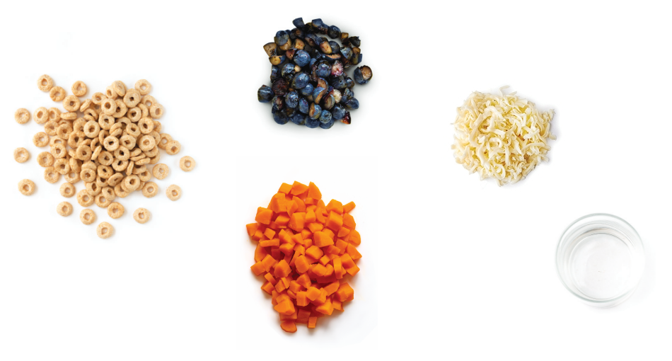 Selection of food ingredients including dry cereal rings, blueberries, shredded cheese, diced carrots, and a glass of water on a white background